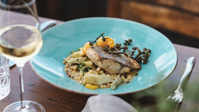 Gebratener Seesaibling, 3erlei Marchfeld Spargel, © Niederösterreich Werbung/Michael Reidinger Gourmetgericht mit Fisch auf blauem Teller, Glas Weißwein daneben.