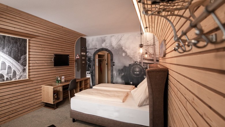 Gasthof Berghof, © Gasthof Berghof/Nici Seiser Hotelzimmer mit Holzwänden, einem Doppelbett und einem großen Wandbild einer Dampflok.