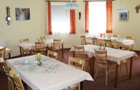 Frühstücksraum, © Pension Caltun Ein gemütlicher Frühstücksraum mit mehreren gedeckten Tischen und Holzstühlen, dekoriert mit Blumen und Bildern an den Wänden.