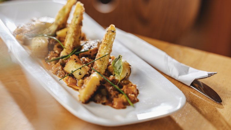 Hier treffen Wirtshausklassiker auf Gourmetmenüs, © Niederösterreich Werbung/Michael Reidinger Gourmetgericht auf weißem Teller mit frittierten Gemüsesticks und Kräutern.