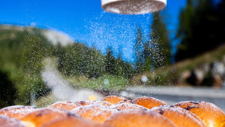 Baumgartnerhütte_Buchteln2(c)Christian Kremsl_G1B6299 (1), © Christian Kremsl Buchteln werden mit Puderzucker bestreut, im Hintergrund eine Berglandschaft.