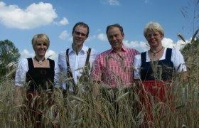 Familie Zimmermann, © Zimmermann Vier Personen in traditioneller Kleidung stehen in einem Getreidefeld unter blauem Himmel.