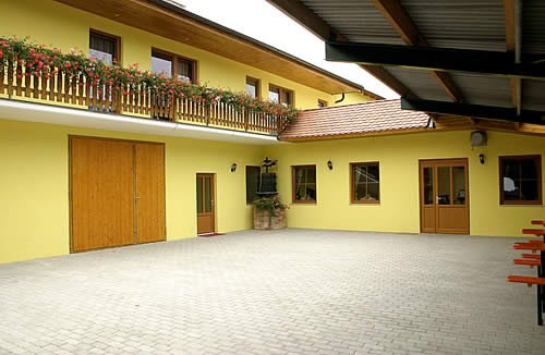 Innenhof, © Berg-Hahn Innenhof eines gelben Gebäudes mit Holztüren und Balkon mit Blumen.