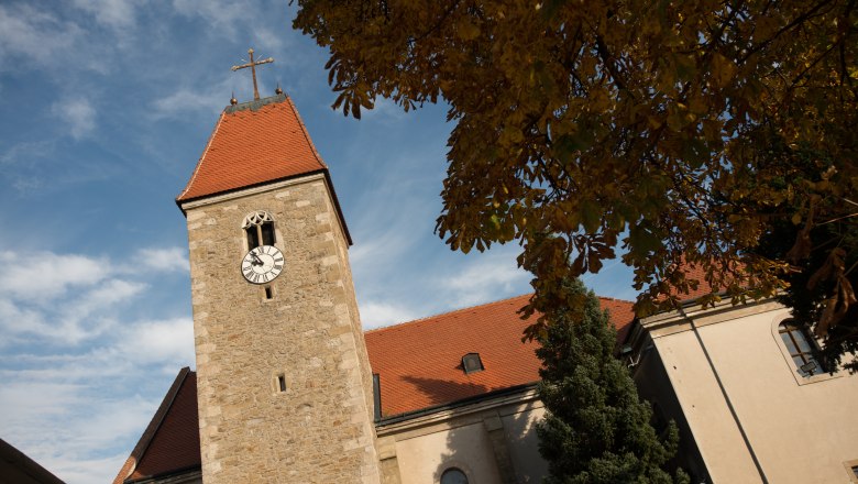 Kirche Weißenkirchen, © dphoto.at Kirchturm der Kirche Weißenkirchen mit Uhr und rotem Dach, umgeben von Herbstlaub und blauem Himmel.