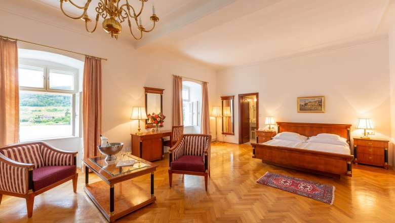 Suite im Hotel Richard Löwenherz, © Chris Saupper Elegante Hotelsuite mit Holzmöbeln, Doppelbett, Sesseln und Ausblick auf die Landschaft.