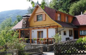 Ferienhaus Bauer in Trattenbach, © Ferienhaus Bauer Ein traditionelles Ferienhaus mit Holzveranda und Schindeldach, umgeben von Bäumen und Bergen.