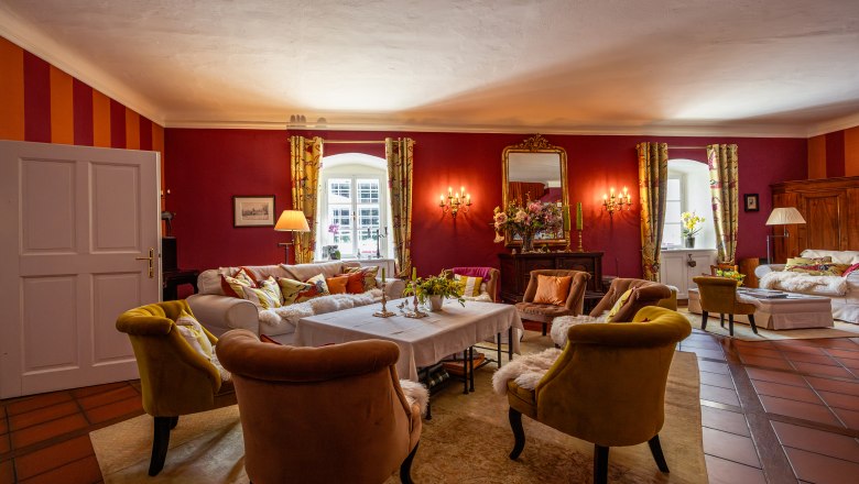 Forsthaus Langschlägerwald, © Niederösterreich Werbung / Maximilian Pawlikowsky Elegantes Wohnzimmer mit roten Wänden, bequemen Sesseln und einem großen Spiegel.