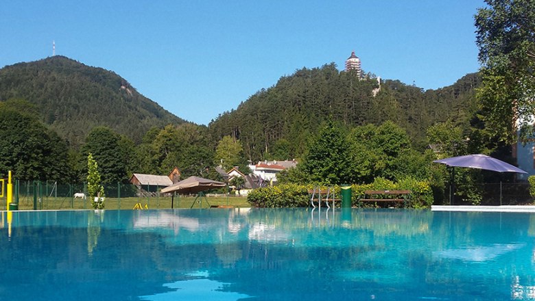Freibad Gutenstein, © Karl Denk Freibad mit Blick auf bewaldete Hügel und einen Turm in der Ferne.