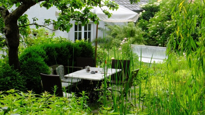 privatgarten-hofbauer_ausschn_dscf3895_c_die-gaerten-niederoesterreichs, © Die Gärten Niederösterreichs Ein idyllischer Garten mit einem Tisch und Stühlen, umgeben von üppigem Grün und einem Baum.