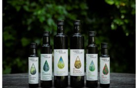 Hagenthaler Ölmanufaktur, © Robert Mussil Sechs Flaschen Hagenthaler Bio-Öle auf einem Holztisch vor grünem Hintergrund.