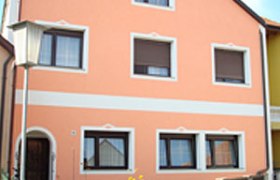 Haus Vorderansicht, © Jeschko Vorderansicht eines zweistöckigen Hauses mit orangefarbener Fassade und weißen Fensterrahmen.