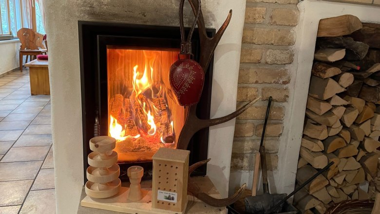 Kamin im Winter spendet wohlige Wärme, © KlammWirtin Ein brennender Kamin mit Holzscheiten, Dekorationen und Holzstapel daneben.