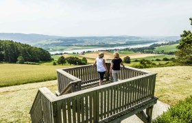 Aussichtswarte am Henzing, © Robert Herbst Zwei Personen stehen auf einer hölzernen Aussichtsplattform mit Blick auf eine weite Landschaft und einen Fluss.
