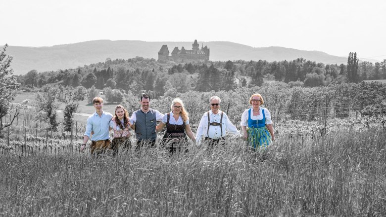 TDR-Hopfeld-Dreikönigshof, © ehnpictures- Johannes Ehn Eine Gruppe von sechs Personen in traditioneller Kleidung steht auf einem Feld mit einer Burg im Hintergrund.