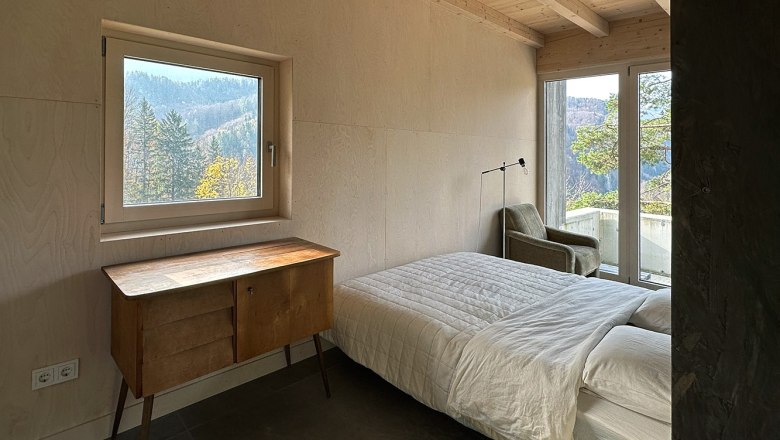 Schlafbereich, © Meinrad Hofer Schlafzimmer mit Bett, Holzdecke, Fenster mit Bergblick und Kommode.
