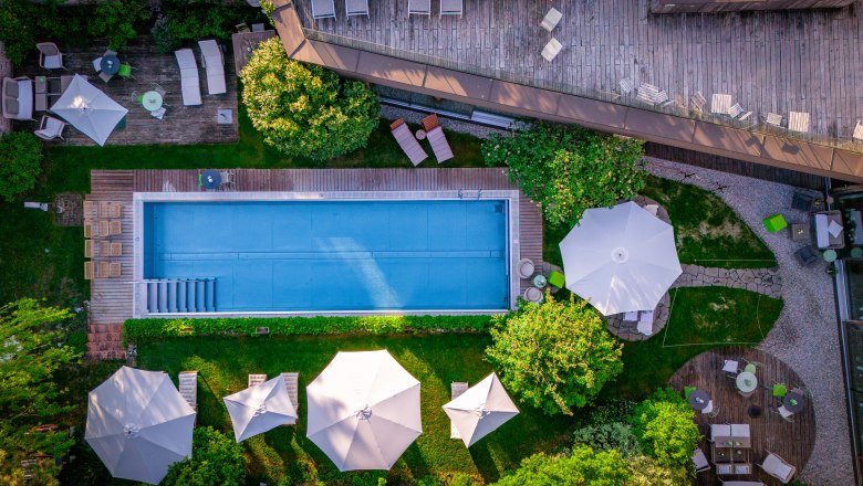 Hotel Landhaus Moserhof, © Niederösterreich Werbung / Maximilian Pawlikowsky Luftaufnahme eines Pools mit umliegenden Liegestühlen und Sonnenschirmen in einem Garten.