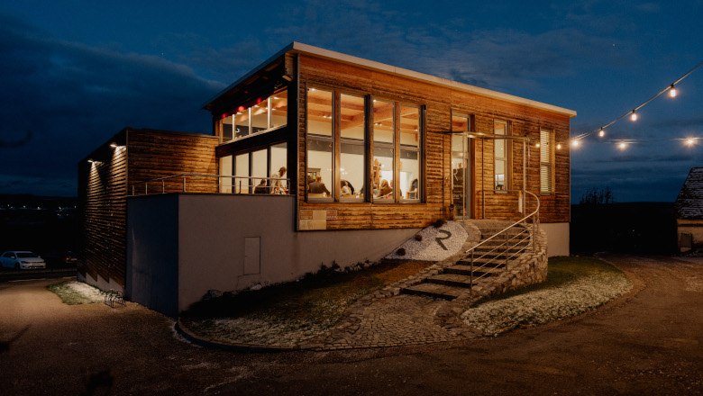 Heurigenlokal außen, © Weingut Rieder Außenansicht eines modernen Heurigenlokals bei Nacht mit beleuchteten Fenstern und Lichterkette.