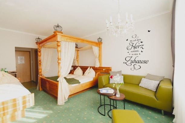 Himmelbettzimmer, © Gasthof Berghof Ein gemütliches Zimmer mit Himmelbett, grüner Couch und Wandtattoo.