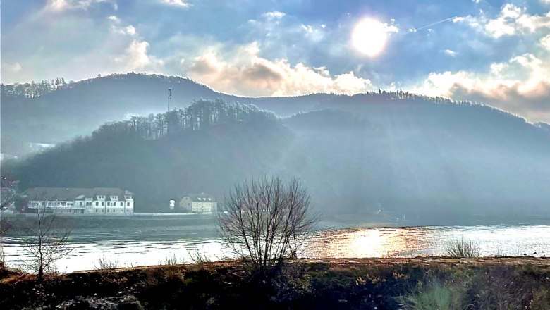 Aussicht vom Haus Donau, © Haus Donau, Hr. Benesics Sonnenstrahlen über einem Fluss mit Hügeln im Hintergrund.