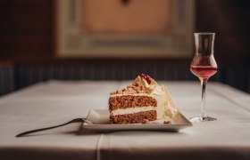 Highlight: Dirndl-Spezialitäten, © Niederösterreich Werbung/Daniela Führer Ein Stück Torte mit Sahne und ein Glas Likör auf einem gedeckten Tisch.