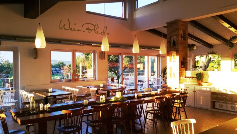 Gastzimmer Müllner Tom, © Helge Wöll Ein gemütliches Gastzimmer mit Holztischen und Stühlen, dekoriert mit Kerzen und Pflanzen, beleuchtet von warmem Sonnenlicht.