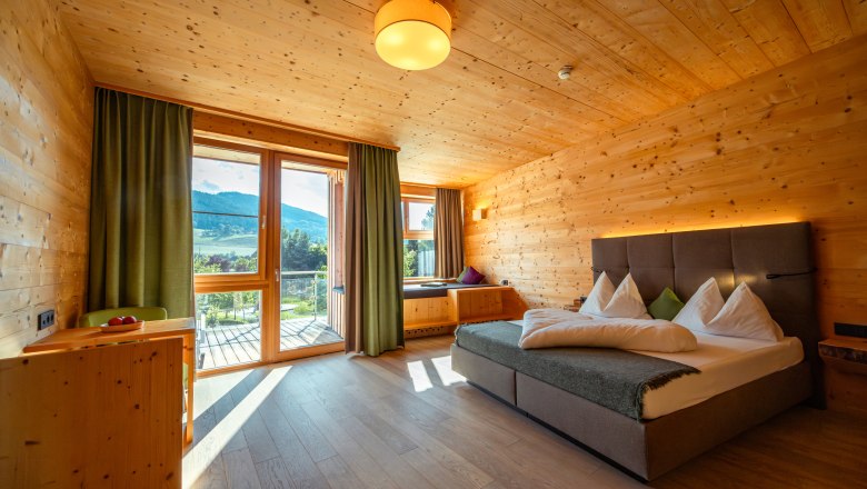 Naturhotel Molzbachhof, © Niederösterreich Werbung / Maximilian Pawlikowsky Hotelzimmer mit Holzwänden, großem Bett und Balkon mit Bergblick.