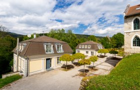 Kavaliershäuser, © Wiener Alpen / Christian Kremsl Zwei Kavaliershäuser mit Mansardendächern und gepflegten Bäumen im Vordergrund, umgeben von grüner Landschaft und blauem Himmel.