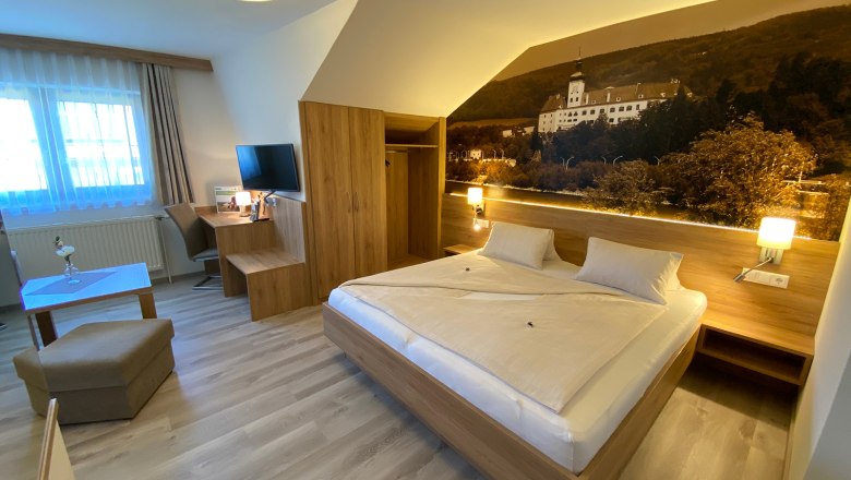 Doppelzimmer Sommer, © Privatzimmer Leeb Modernes Hotelzimmer mit Doppelbett, Schreibtisch, Fernseher und großem Wandbild.