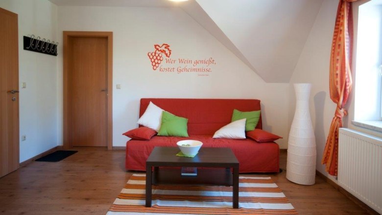 Gästezimmer, © Familie Rain Gemütliches Gästezimmer mit rotem Sofa, Kissen, Lampe und Wandzitat.