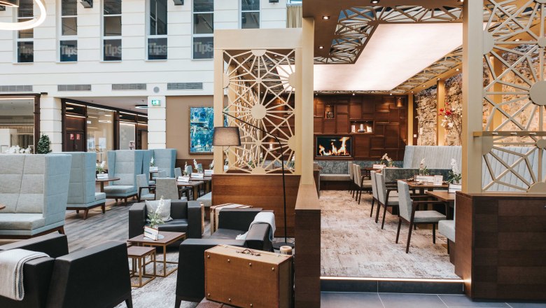 Café Wohnzimmer Innenansicht, © FMS Steinertor Gastronomie BetriebsgmbH Innenansicht eines modernen Cafés mit gemütlichen Sitzbereichen, Kamin und stilvoller Dekoration.