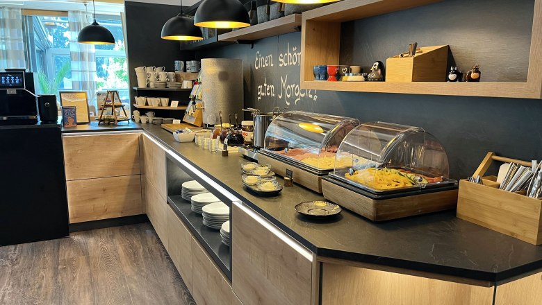 Frühstücksbuffet, © Café Pension Kristall Ein Frühstücksbuffet mit verschiedenen Speisen, Geschirr und einer Kaffeemaschine in einem modernen Raum.