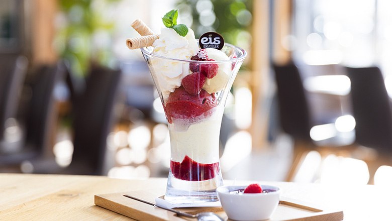 Ein Eisbecher mit Fruchteis, Schlagobers, Waffeln und Himbeeren auf einem Holzbrett., © Blochberger Eisproduktion GmbH Ein Eisbecher mit Fruchteis, Schlagobers, Waffeln und Himbeeren auf einem Holzbrett., © Blochberger Eisproduktion GmbH