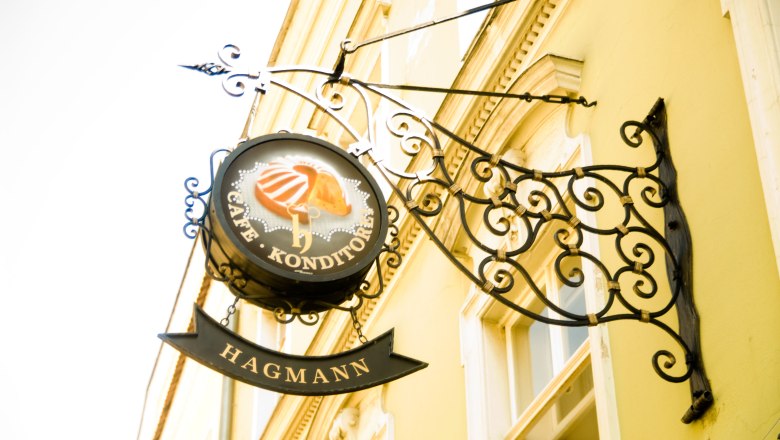 Konditorei Hagmann, © Konditorei Hagmann Metallschild 'Café Konditorei Hagmann' an einer gelben Hauswand.