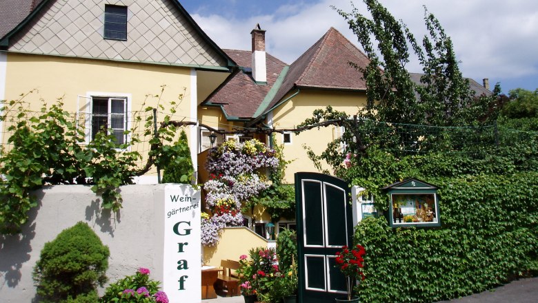 Aussenansicht, © Familie Graf Außenansicht eines gelben Gebäudes mit Pflanzen und Blumen.