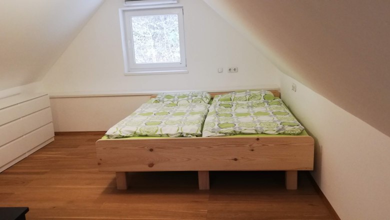 Doppelbett, © Günter Lammer Ein Dachgeschosszimmer mit einem Doppelbett aus Holz und grüner Bettwäsche, daneben eine weiße Kommode.