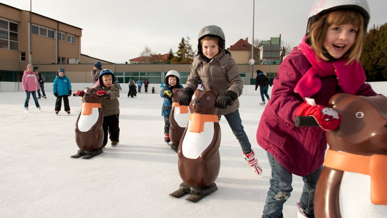 Kunsteisbahn Matzen, © Barbara P. Photography Kinder beim Schlittschuhlaufen mit Pinguin-Hilfen auf einer Eisbahn.