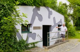 Erdstallmuseum Althöflein, © Marktgemeinde Großkrut Eingang des Erdstallmuseums Althöflein mit einem Mann, der die Tür zeigt.