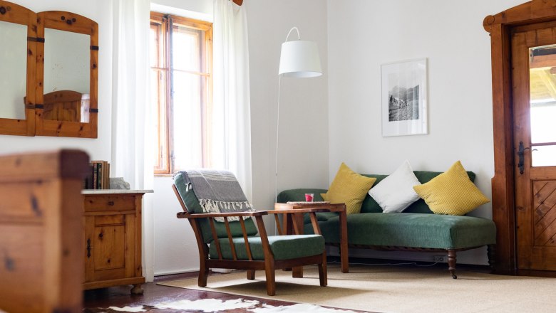Besonderes Sommerfrische-Flair in den Zimmern, © Wiener Alpen - Lierzer Gemütliches Wohnzimmer mit Holzmöbeln, grünem Sofa, gelben Kissen und Kuhfell-Teppich.