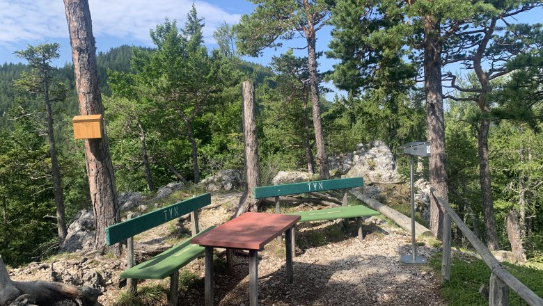 Blickplatz Luckerte Wand, © TVB Semmering-Rax-Schneeberg Ein Rastplatz im Wald mit zwei Bänken und einem Tisch, umgeben von Bäumen und Felsen.