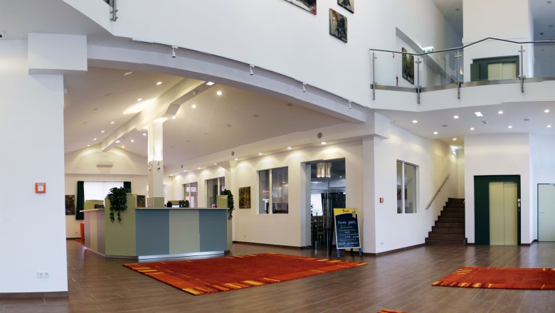 winrooms-03, © Winrooms Betriebs GmbH Moderne Hotellobby mit Rezeption, roten Teppichen und Kunstwerken an den Wänden.