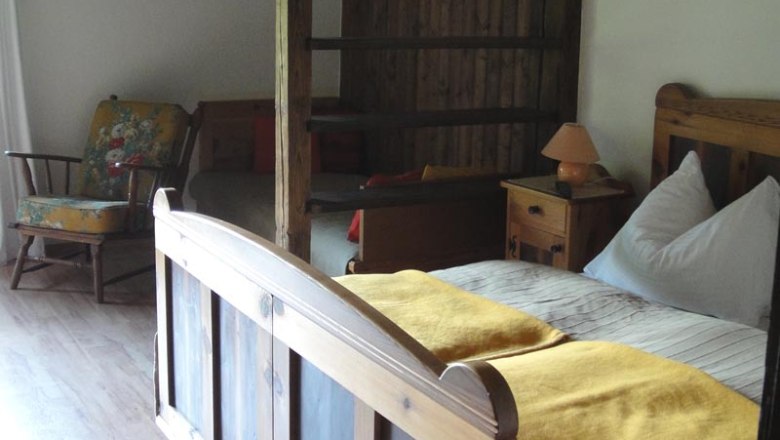 Zimmer Bauernstube, © Familie Kellner Rustikales Zimmer mit Holzbett, gelber Decke, Schaukelstuhl und Holzwänden.