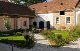 Innenhof, © Franz Böck Ein idyllischer Innenhof mit Kieswegen, grünen Pflanzen und einem Sitzbereich unter einem Metallbogen.