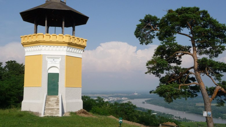 Donauwarte Egelsee, © www.oetk.at Ein gelber Aussichtsturm mit dunklem Dach steht auf einem Hügel mit Blick auf den Fluss Donau und eine Stadt im Hintergrund.