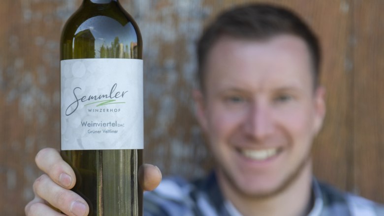 Winzerhof Semmler, © Winzerhof Semmler Ein Mann hält eine Flasche Wein vom Winzerhof Semmler in die Kamera.