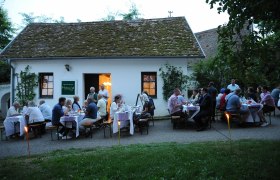 Keller vom Weingut Honsig, © H. Schleich Menschen sitzen abends vor einem Weinkeller und genießen ein Essen im Freien.