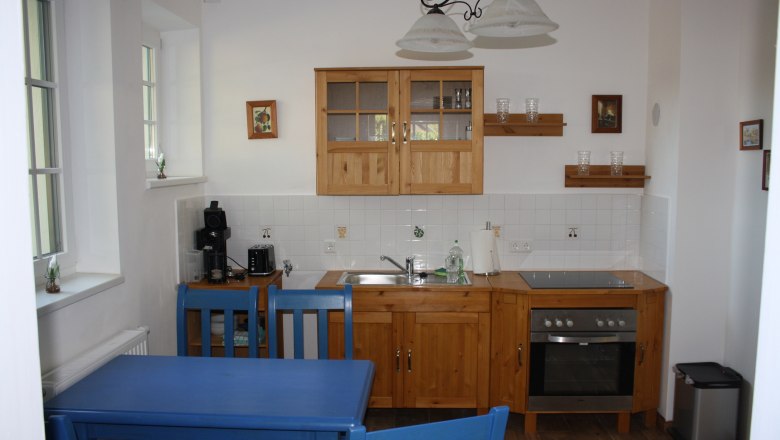 Küche in der Ferienwohnung am Bioweingut Schmidl, © Weingut Schmidl Küche in einer Ferienwohnung mit Holzmöbeln, blauen Stühlen und moderner Ausstattung.