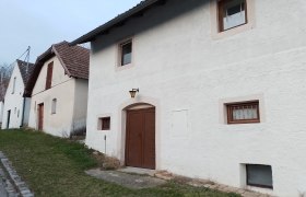 Außenansicht, © Wein-Bleibe Reihen von weißen Häusern mit braunen Türen und Fenstern, entlang einer Straße mit Grasstreifen.