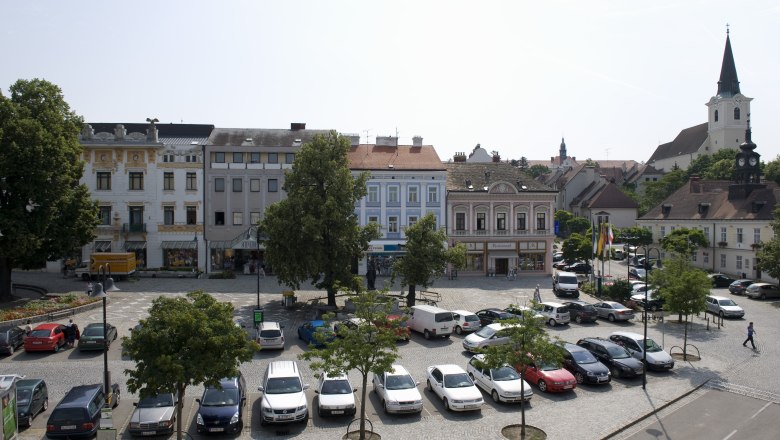 Hollabrunn, © Gemeinde Hollabrunn Stadtplatz in Hollabrunn mit geparkten Autos, historischen Gebäuden und einer Kirche im Hintergrund.