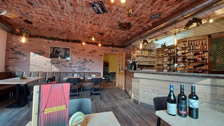 Neue Gaststube - Wirtshaubühne Bernhart, © Wirtshausbühne Bernhart Gemütliche Gaststube mit Holztischen, Bar und Weinflaschen.