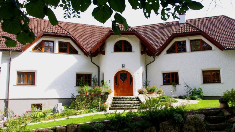 Naturpension ARTNER, © ARTNER Ein großes, weißes Haus mit rotem Ziegeldach und gepflegtem Garten, umgeben von Bäumen.